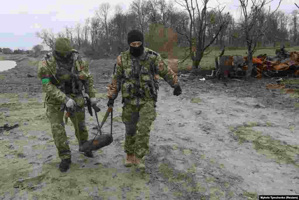 Украинские саперы несут неразорванный снаряд от уничтоженного танка возле села Мотыжин к западу от Киева, 10 апреля 2022 года