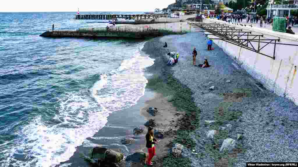 На пляже под набережной Алушты купающихся нет. Люди предпочитают сидеть возле берега