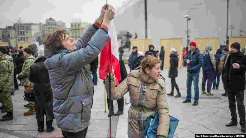 Люди прикрепляют украинскую ленточку на польский флаг